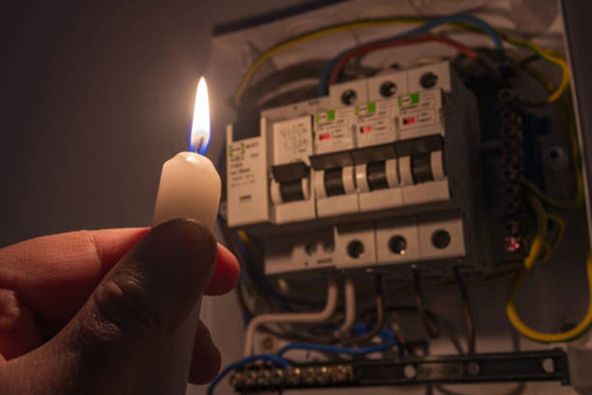 Una mano sostiene una vela frente a la fuente de energía eléctrica ante un corte de luz en su casa.
