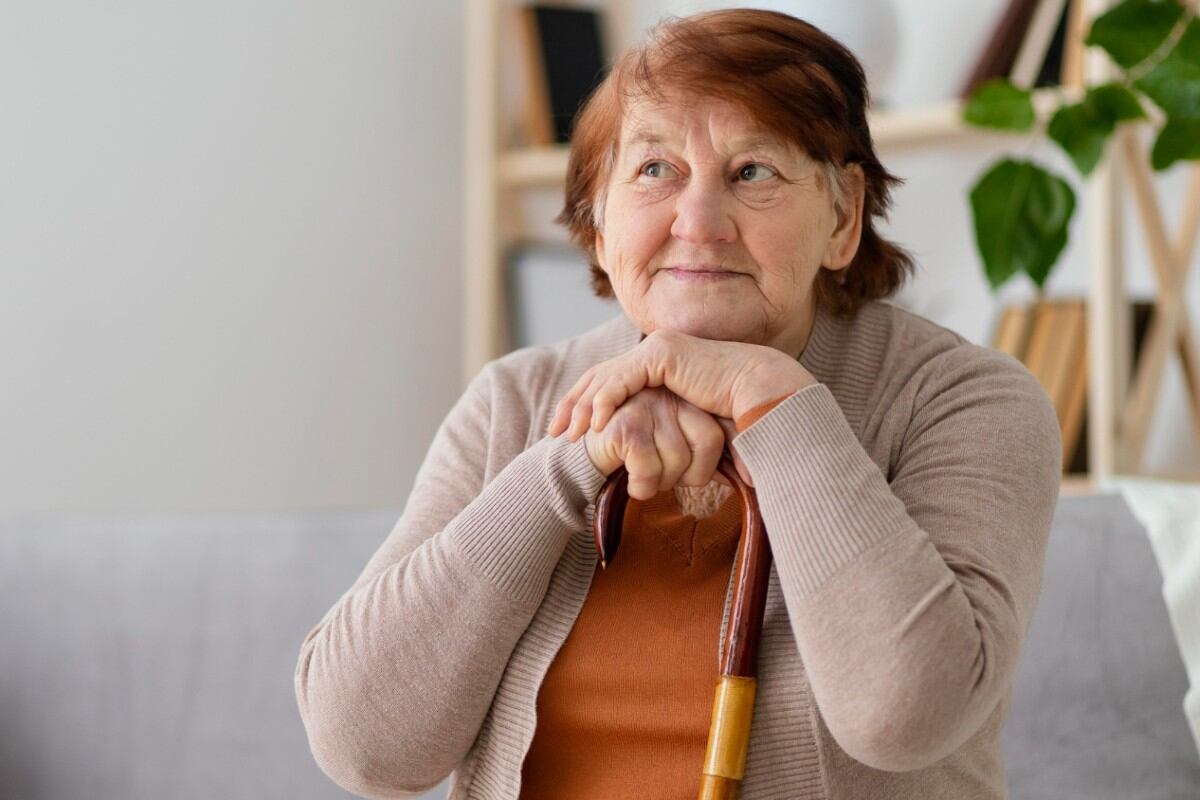 Mujer adulta mayor sentada y apoyada sobre un bastón.