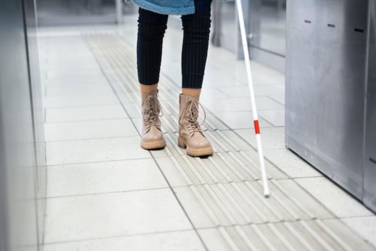 Piernas de una persona con un bastón de ciegos por delante caminando por la calle.