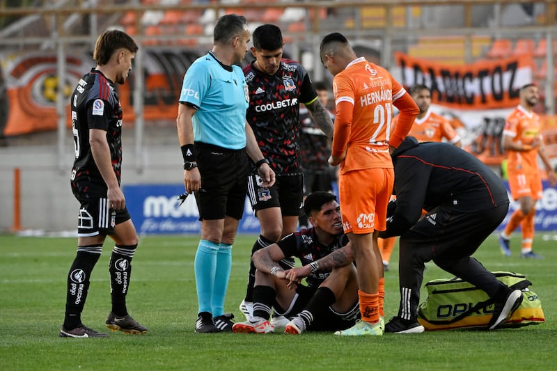 El futbolista Carlos Palacios sentado en la cancha del Estadio Zorros del Desierto rodeado por jugadores de Colo Colo y Cobreloa.