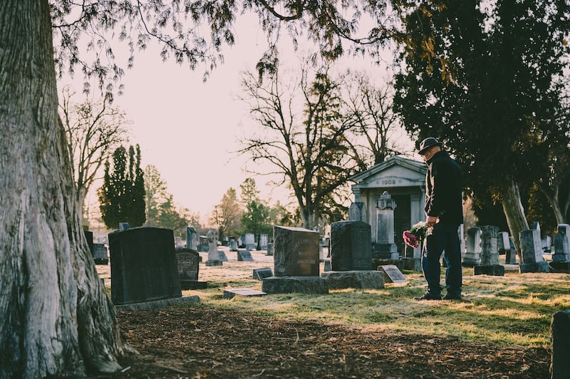 Hombre de pie frente a una sepultura en un cementerio.