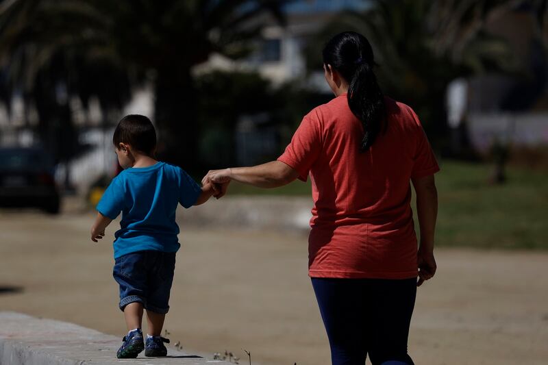 Madre junto a su hijo pequeño caminando por un parque.